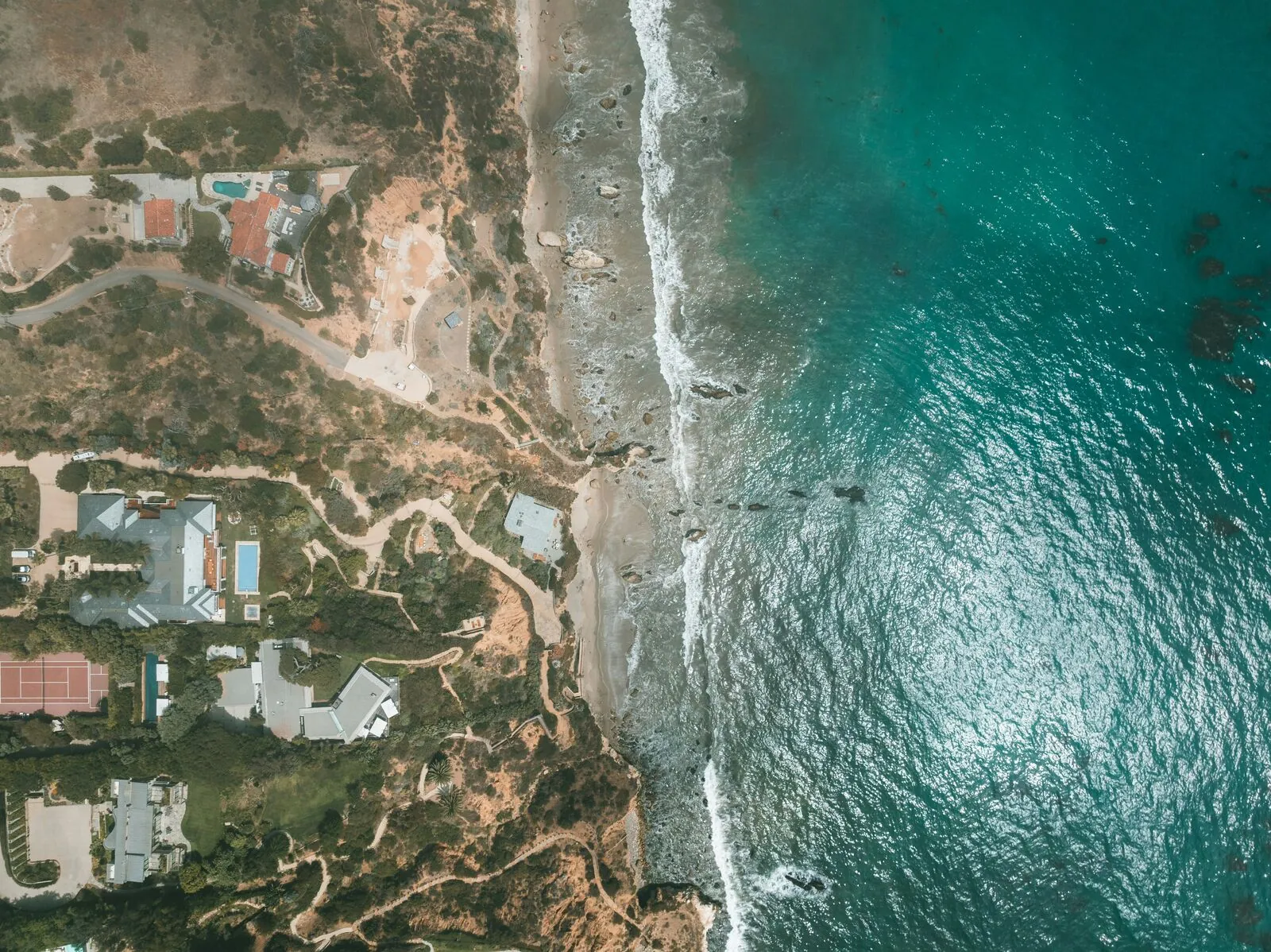 Aerial view of luxury estates along the Malibu coastline with turquoise Pacific Ocean