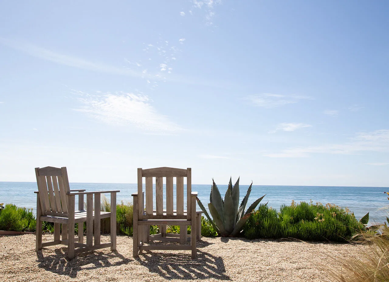 Two weathered teak chairs overlooking the Pacific Ocean from a Malibu beachfront garden
