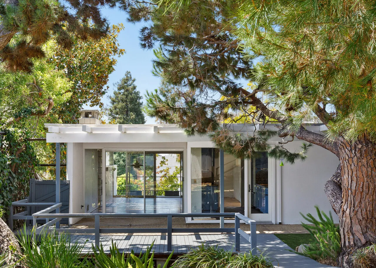 Glass-walled mid-century modern home with open-air patio surrounded by mature pines in Pacific Palisades