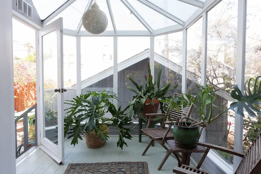 Glass conservatory sunroom filled with tropical plants in an eclectic Venice bungalow